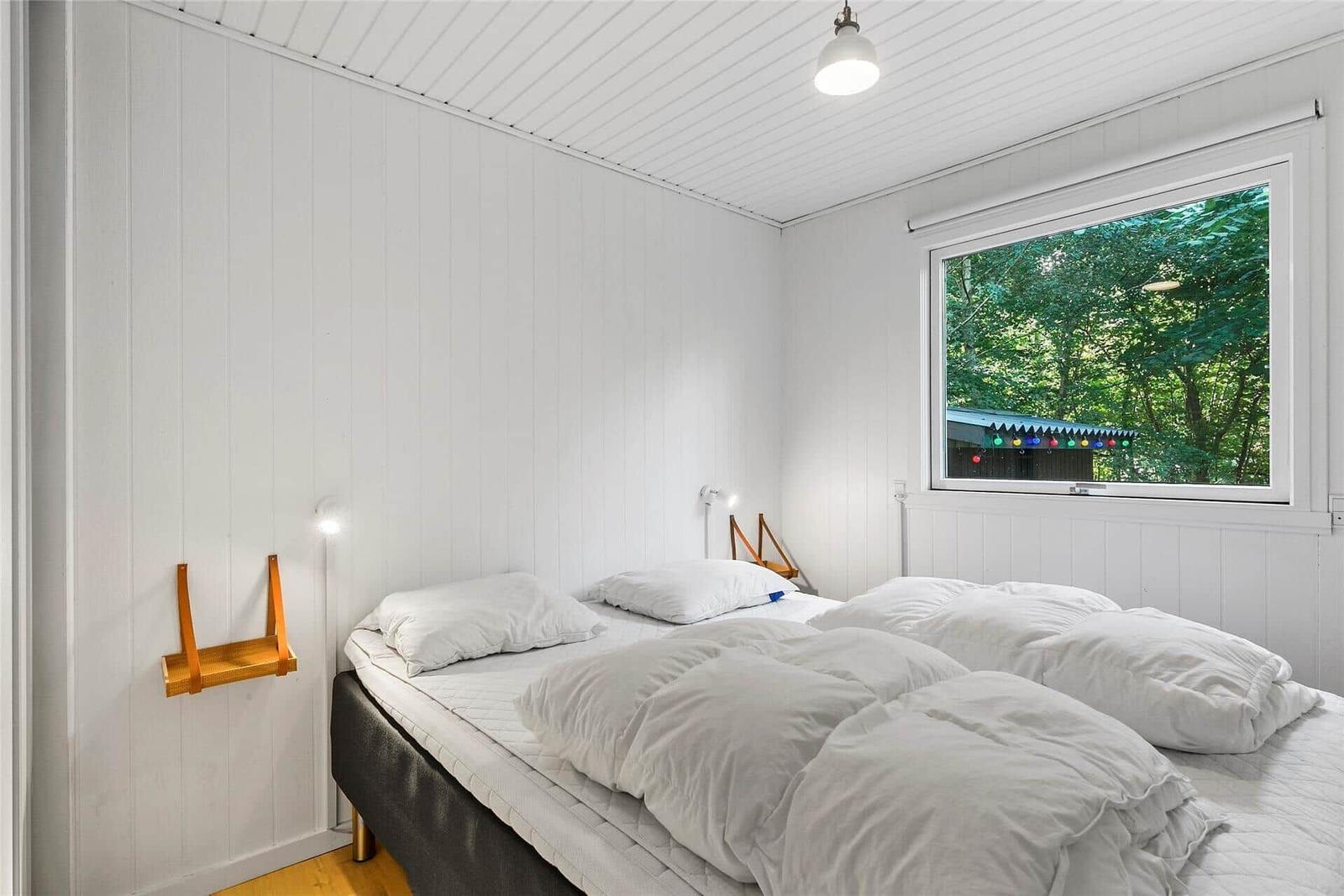 Schlafzimmer mit Bett, Fenster und Wandregal. Holzfußboden und weiße Wände.