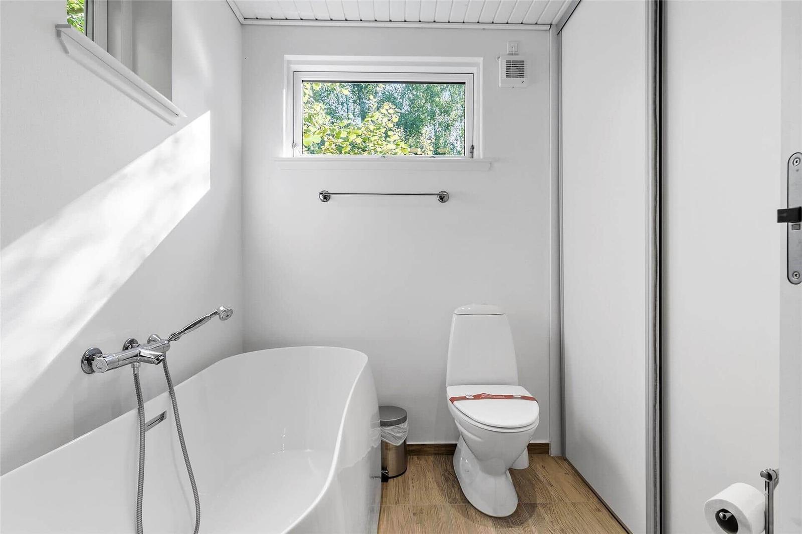 Badezimmer mit Badewanne, Toilette und Fenster zum Wald.