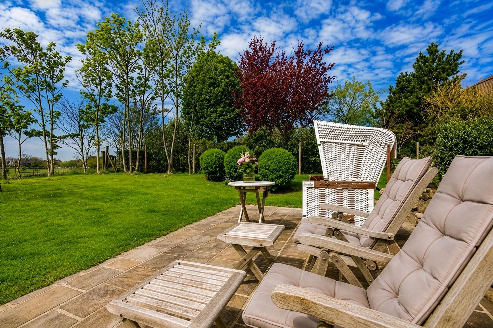 Terrasse mit Liegestühlen und Tisch. Grünfläche und Bäume im Hintergrund.