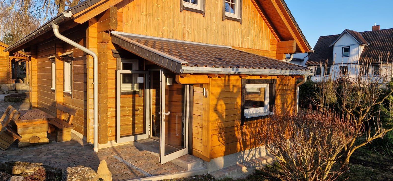 Holzhaus mit Eingangstür und Veranda. Außenbereich mit Bank und Steinpflaster.