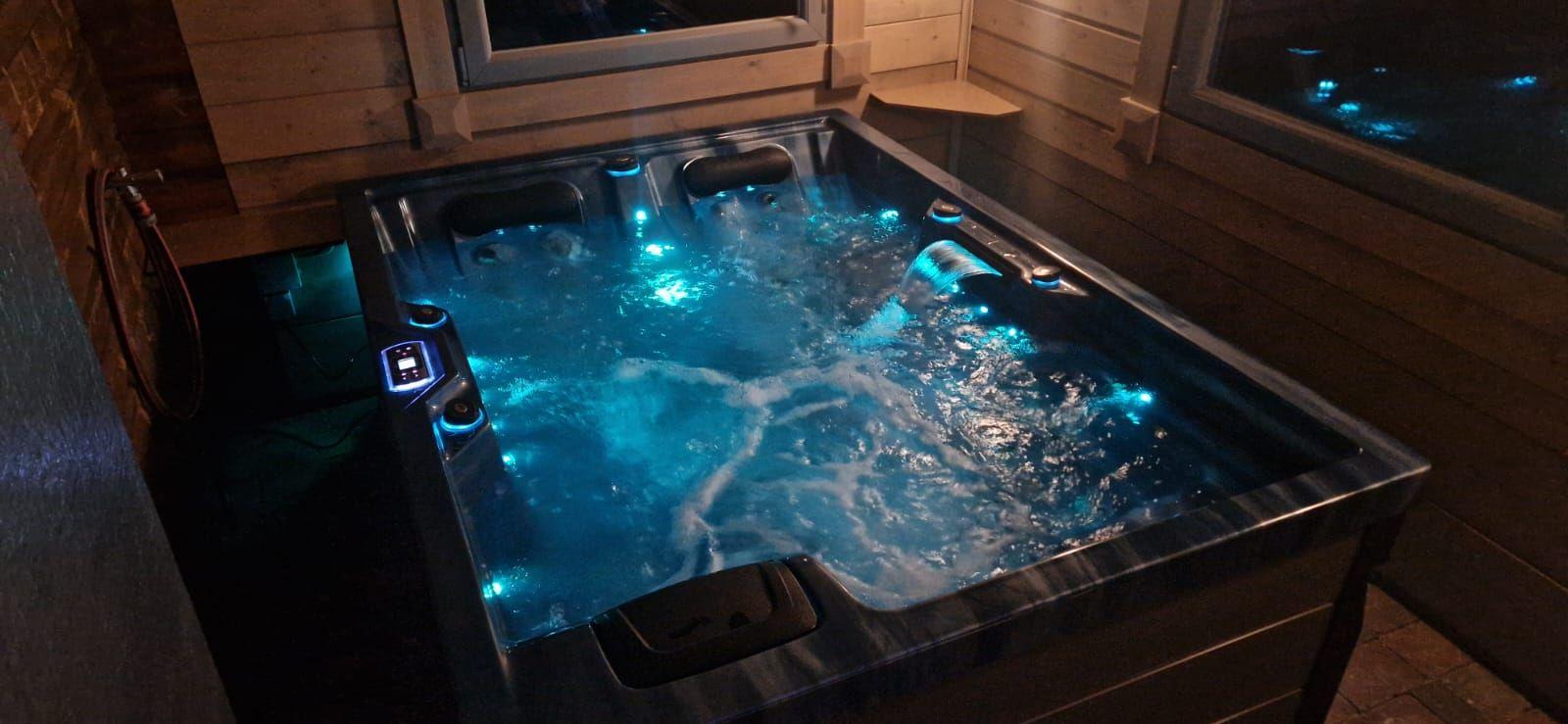 Ein beleuchteter Whirlpool mit blauen Lichtern und Wasserströmungen in einem Holzhaus.
