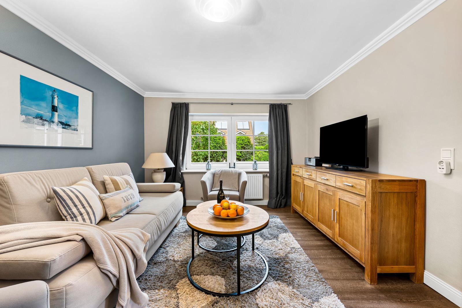 Wohnzimmer mit Sofa, Fernseher und Fenster mit Blick auf Grün.
