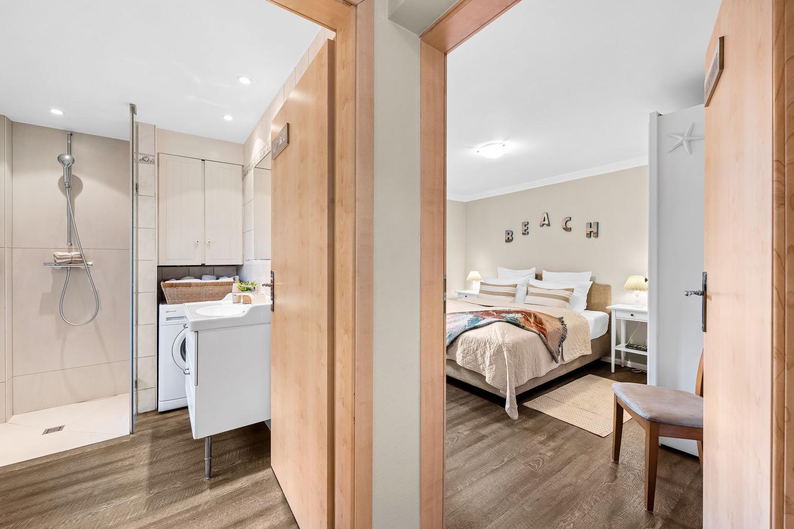 Schlafzimmer mit Bett und Wanddekoration. Nebenraum mit Dusche und Waschmaschine.