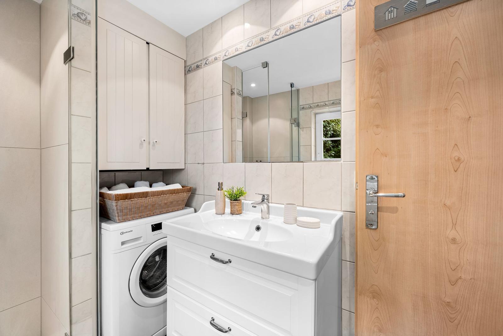 Badezimmer mit Waschmaschine, Spiegelschrank und Holztür.