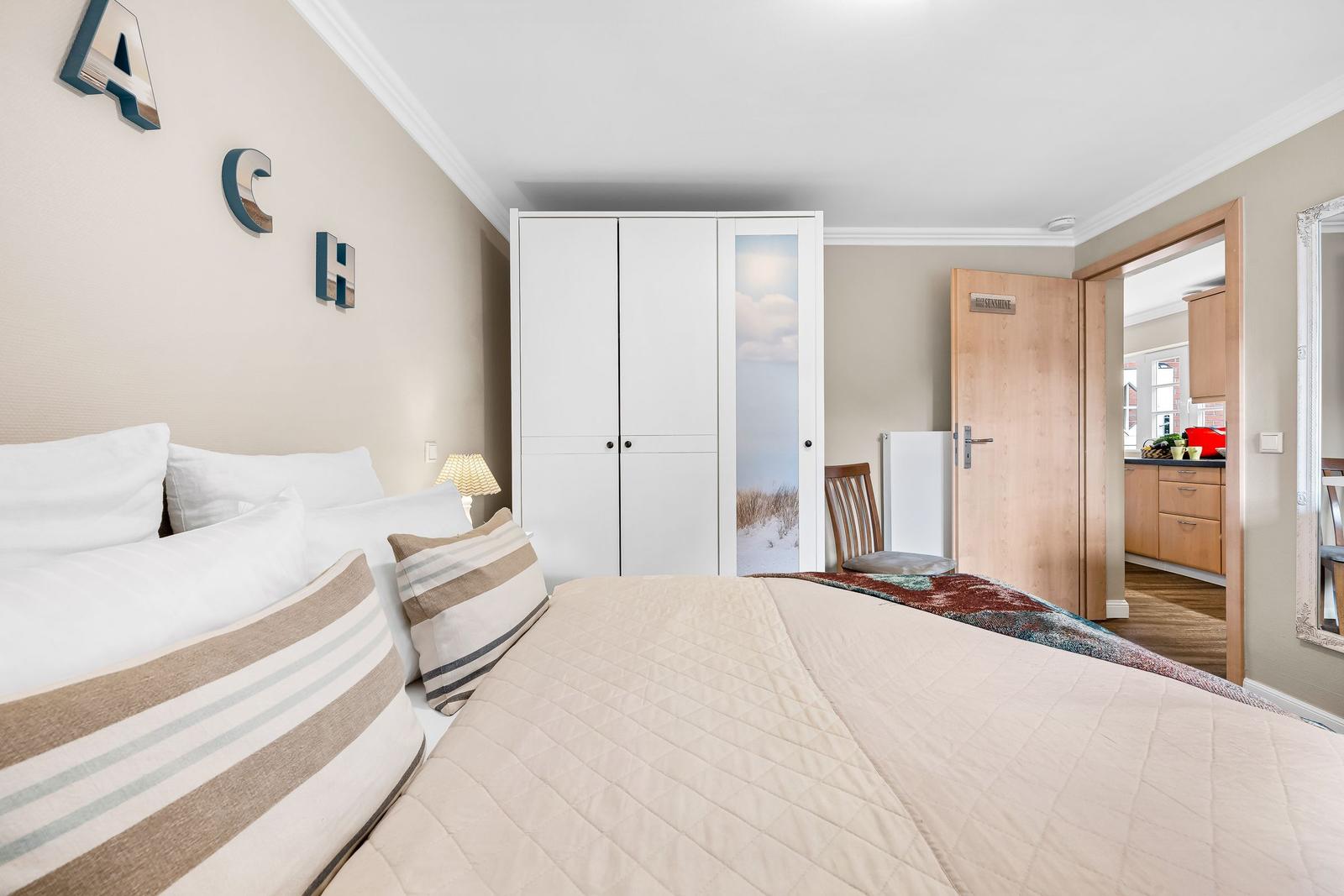 Schlafzimmer mit Bett, Kleiderschrank und Sicht auf Küche.