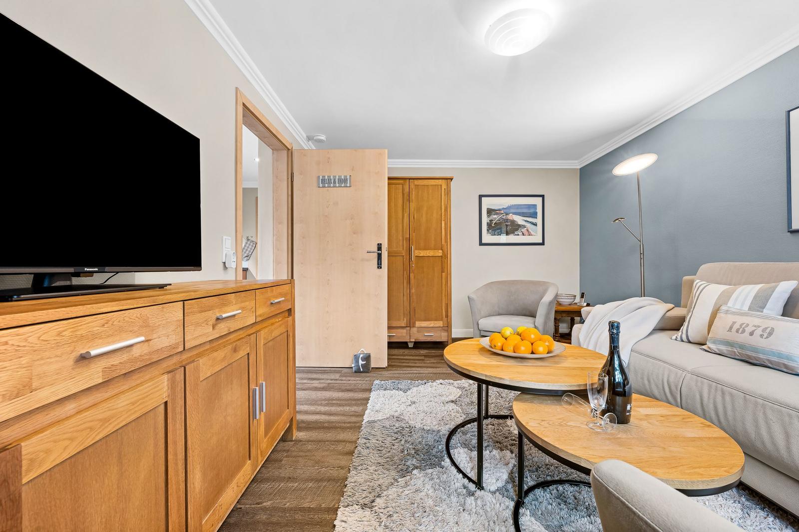 Wohnzimmer mit Sofa, Couchtisch und Fernseher. Hintergrund: Tür und Kleiderschrank.