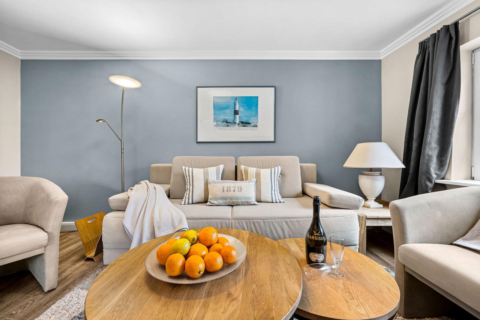 Wohnzimmer mit Sofa, Kissen, Tisch mit Obst und Flasche.