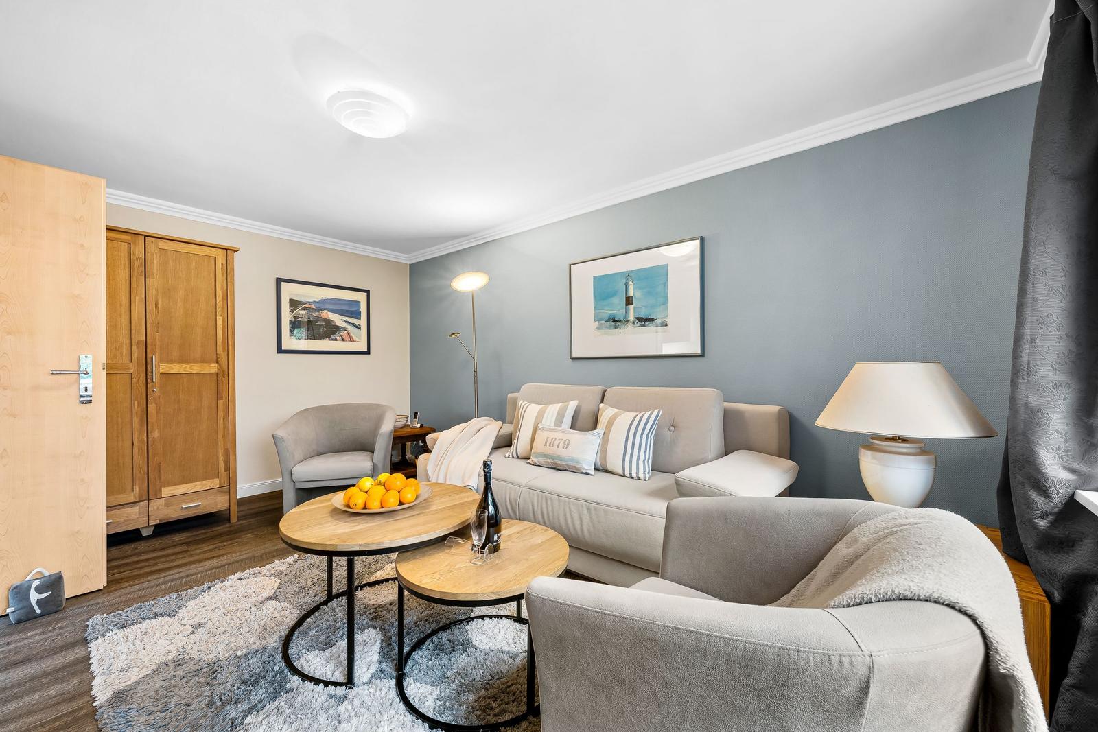 Wohnzimmer mit Sofa, Sesseln, Tisch und Wandbildern.