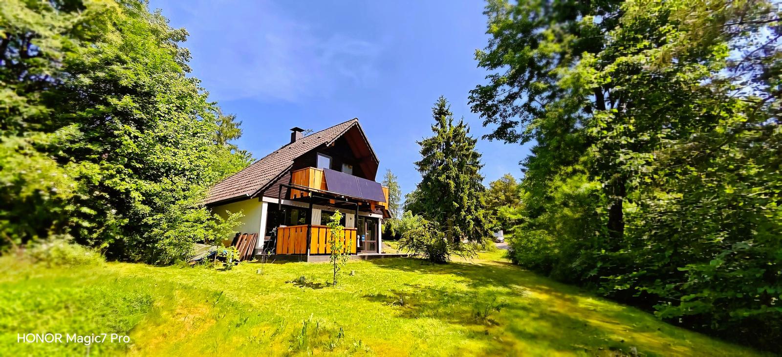 Haus mit Holzveranda und Solaranlage in grüner Umgebung.