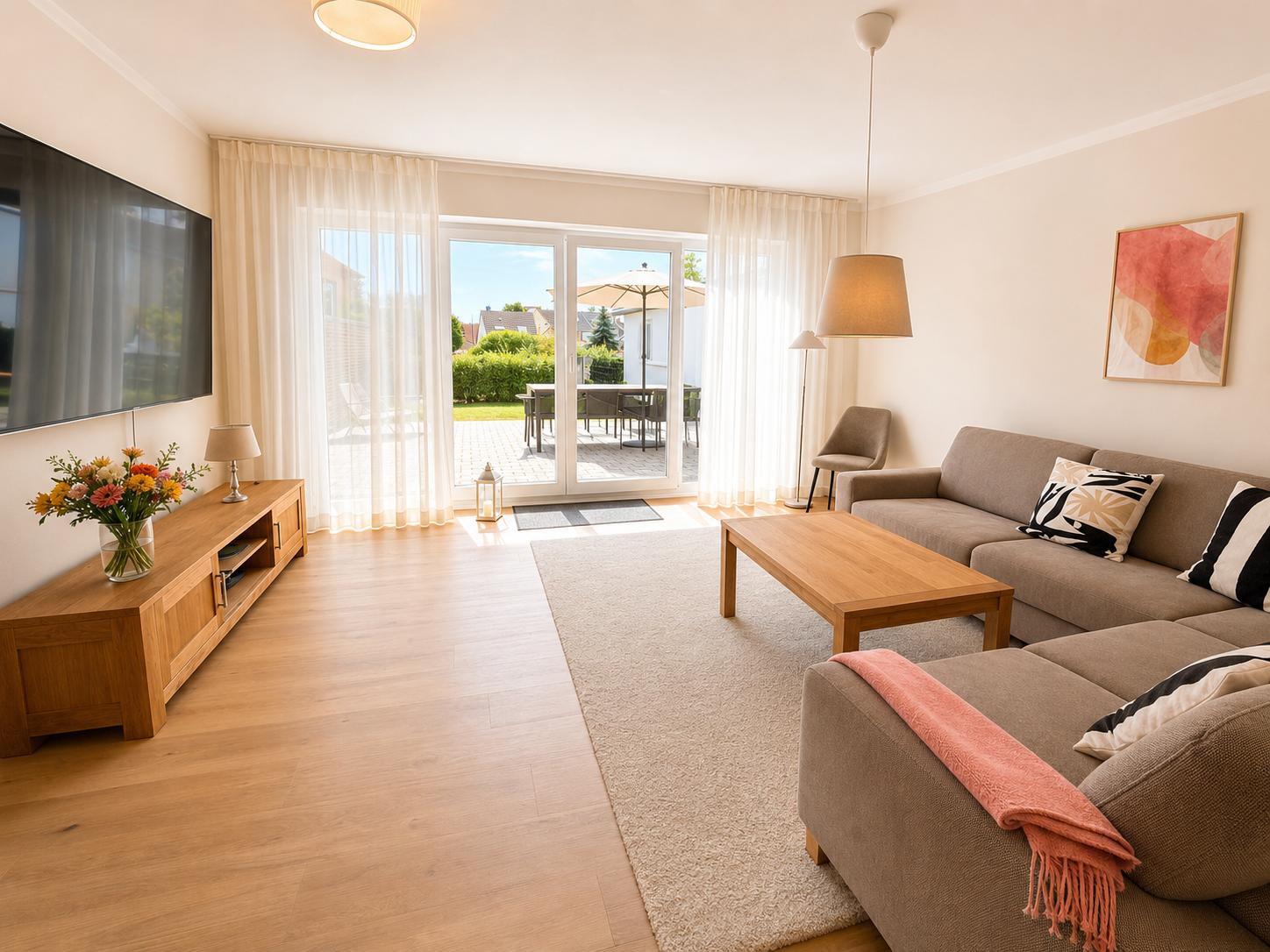 Wohnzimmer mit Sofa, Couchtisch und TV. Durchgang zum Garten mit Sitzgelegenheit.