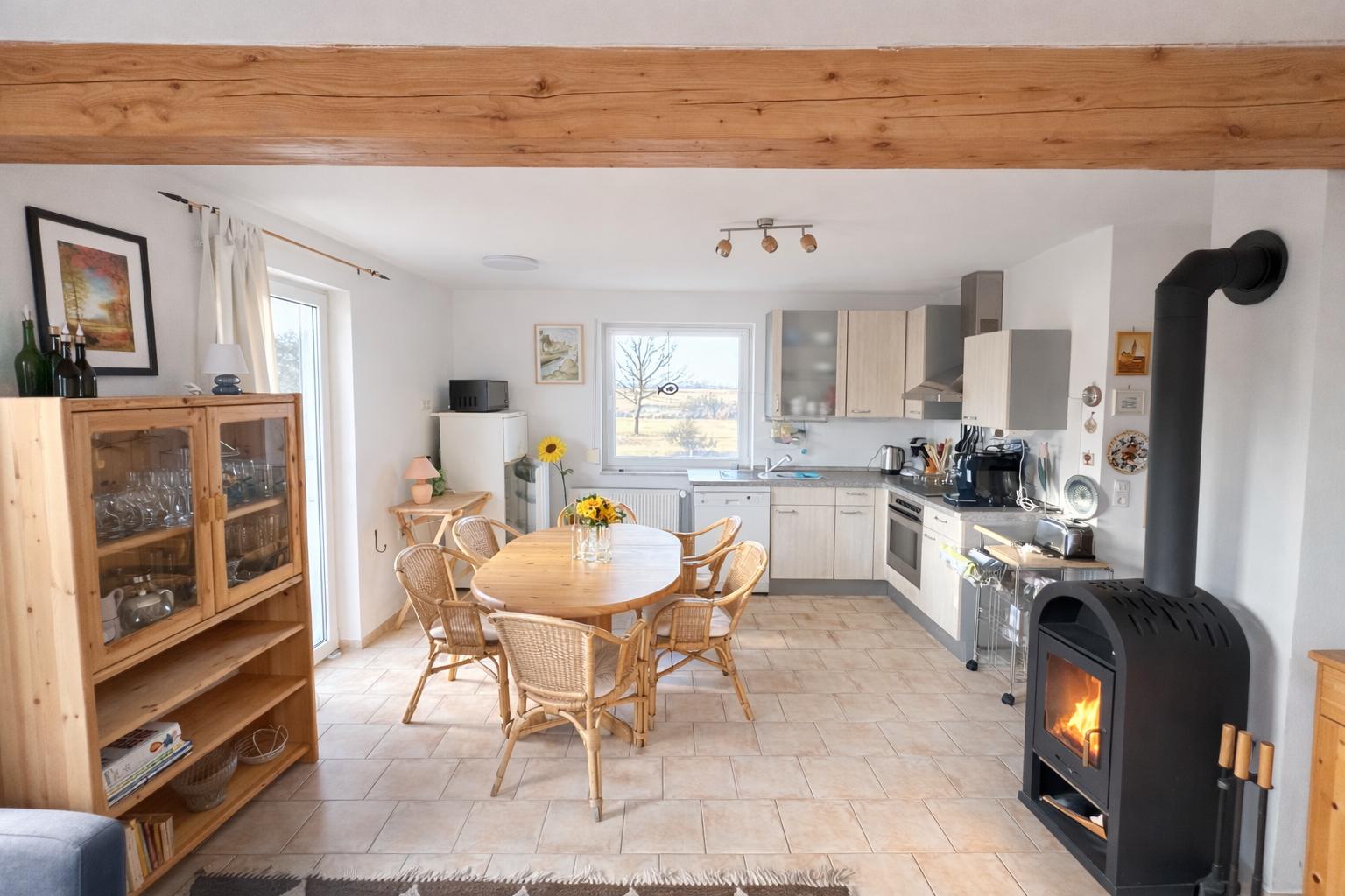 Essbereich mit Holztisch, Stühlen und Küchenbereich mit Ofen und Kamin.