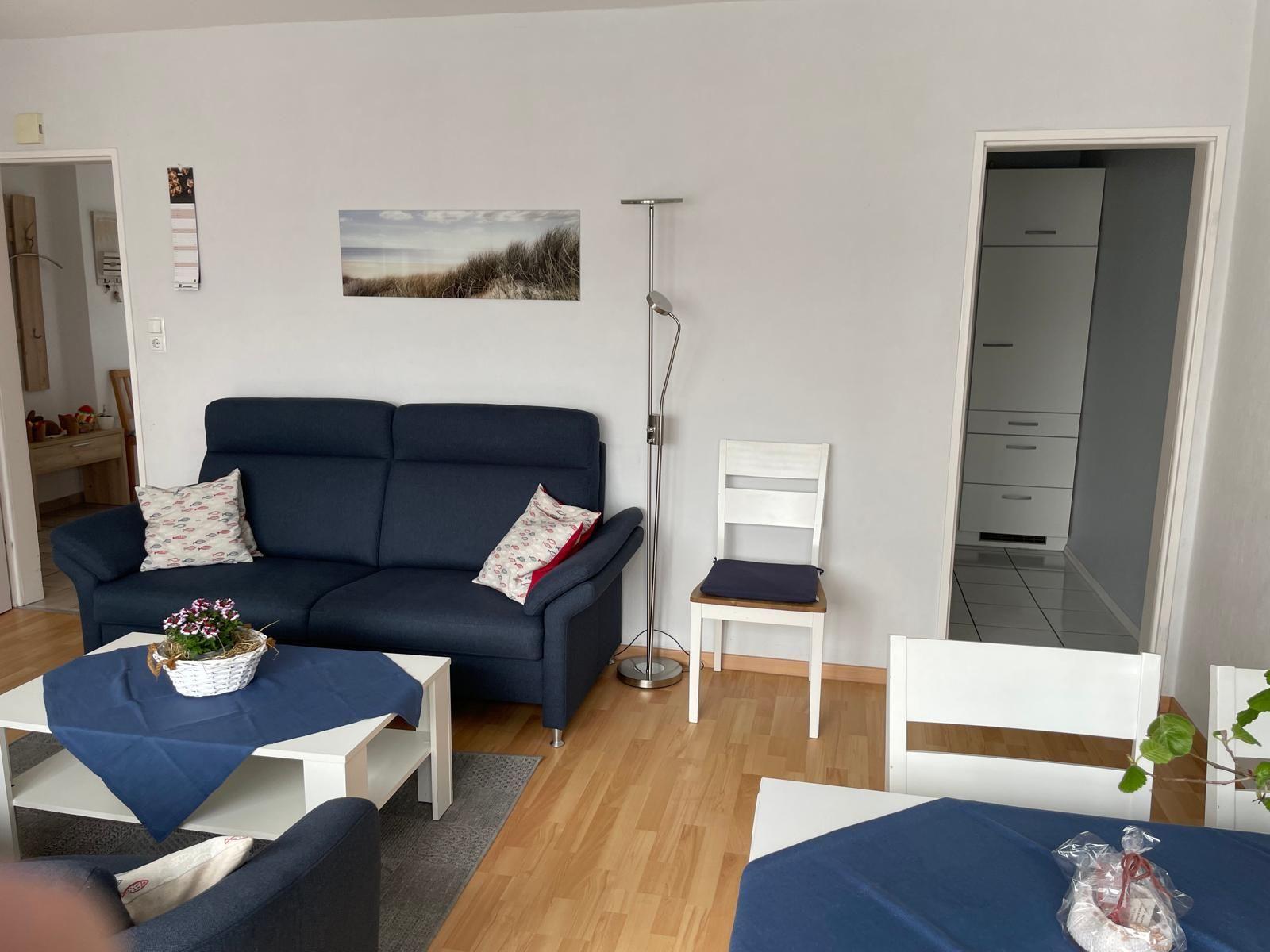 Wohnzimmer mit Sofa, Tisch und Stühlen. Durchgang zu Küche und Flur.