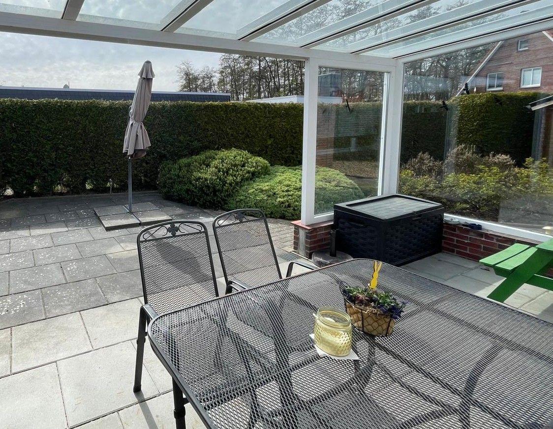Terrasse mit Tisch, Stühlen und Sonnenschirm unter Glasdach.