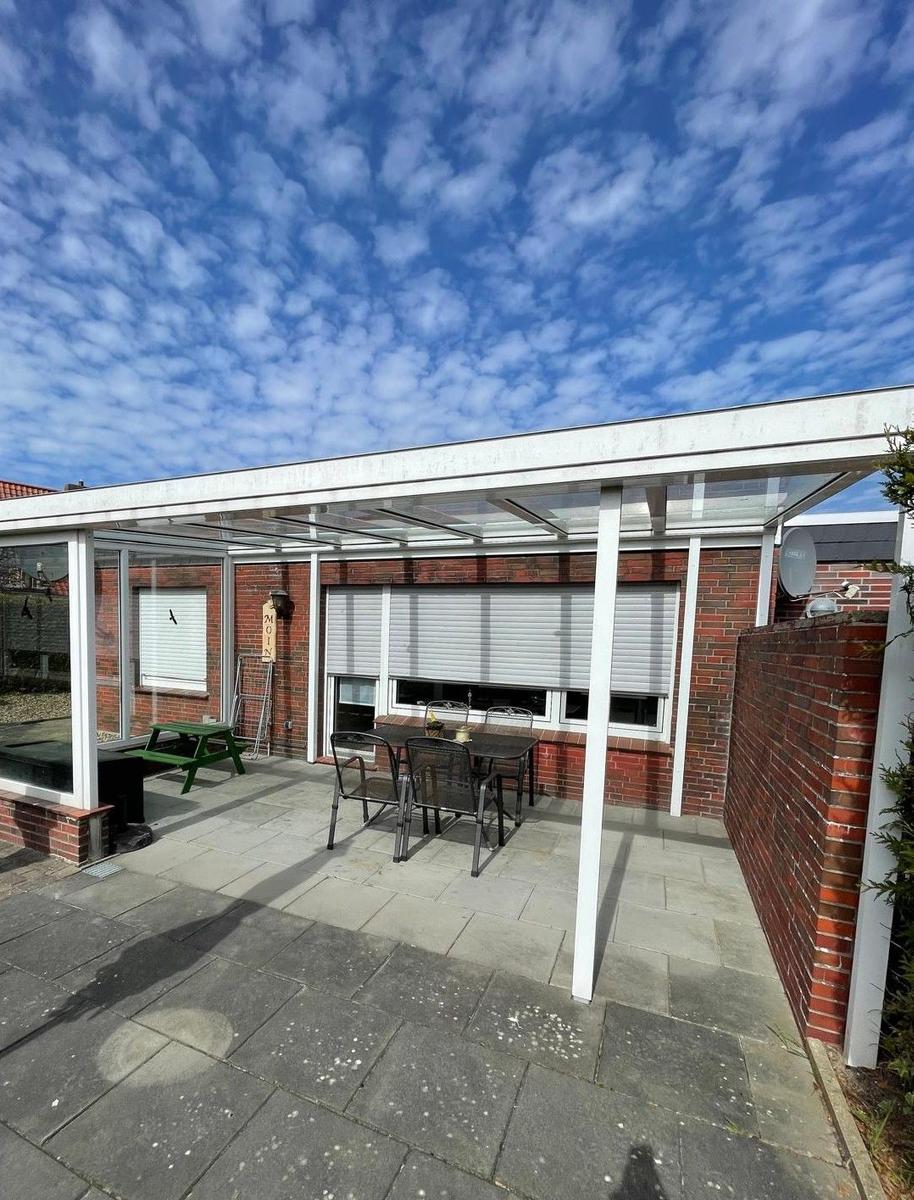 Terrasse mit Sitzgruppe und Pavillon unter blauem Himmel mit Wolken.