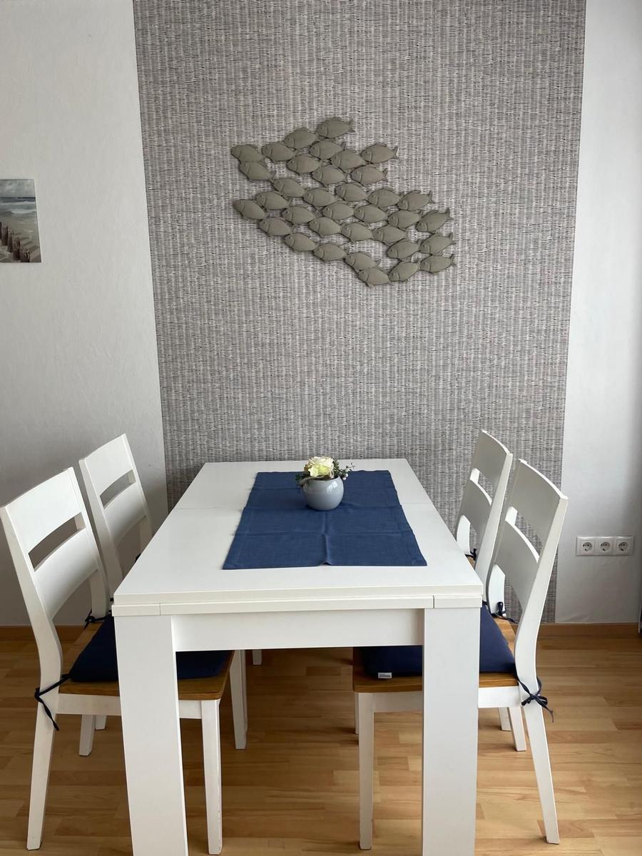 Esszimmer mit weißem Tisch, vier Stühlen und Wanddekoration aus Fischen.