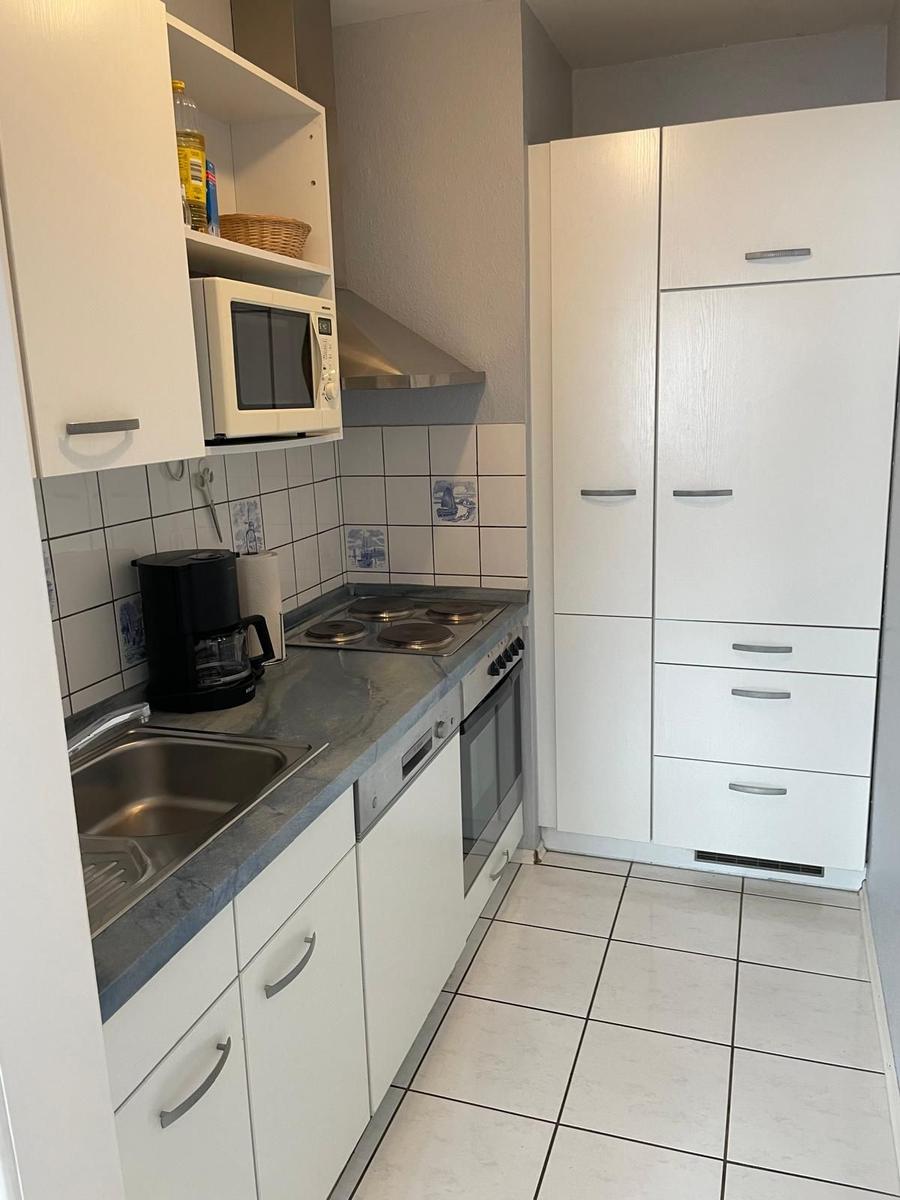 Küche mit weißen Schränken, Kochfeld, Spüle und Mikrowelle.