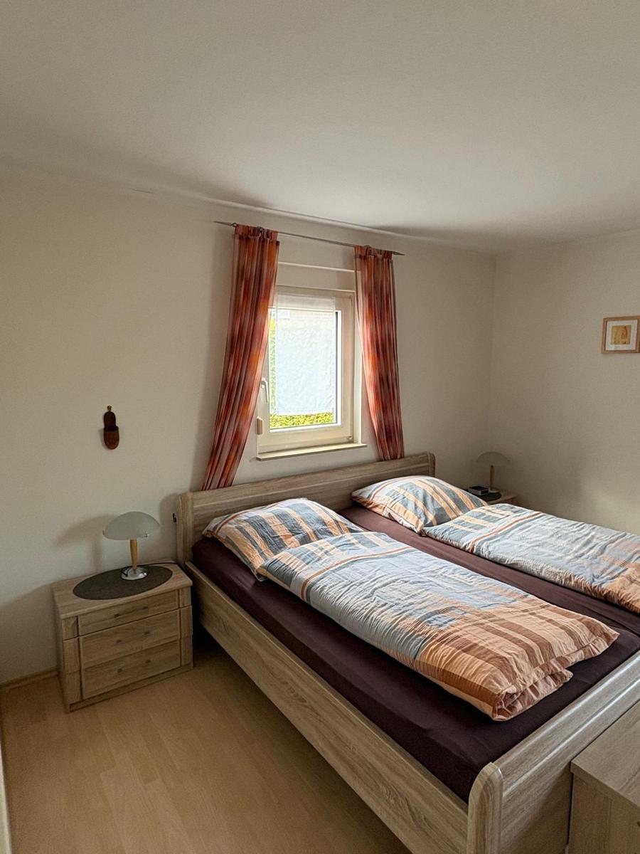 Schlafzimmer mit Doppelbett, Nachttisch und Fenster mit Vorhängen.