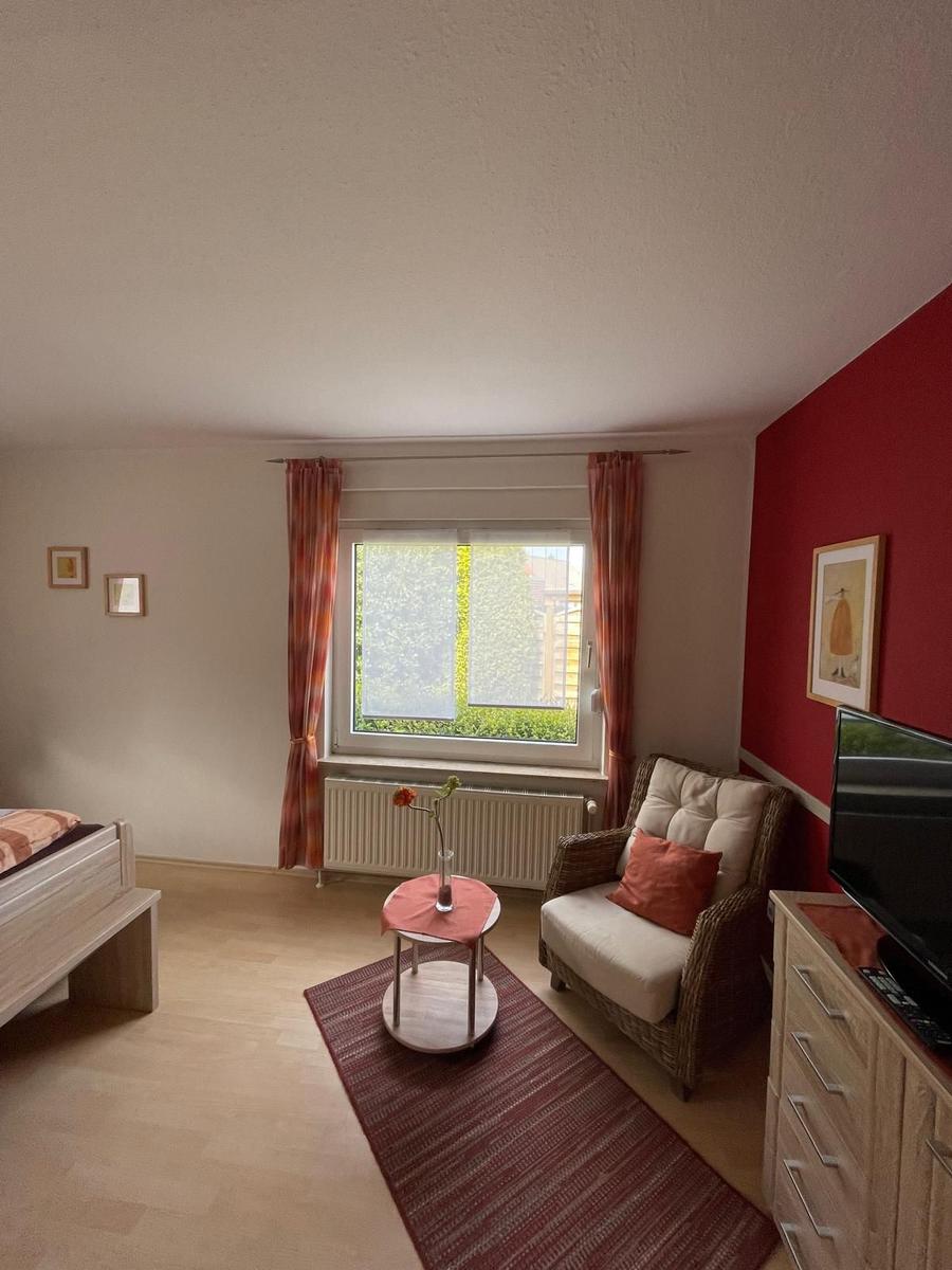 Ein Zimmer mit Bett, Sessel, Fenster und TV-Möbel.