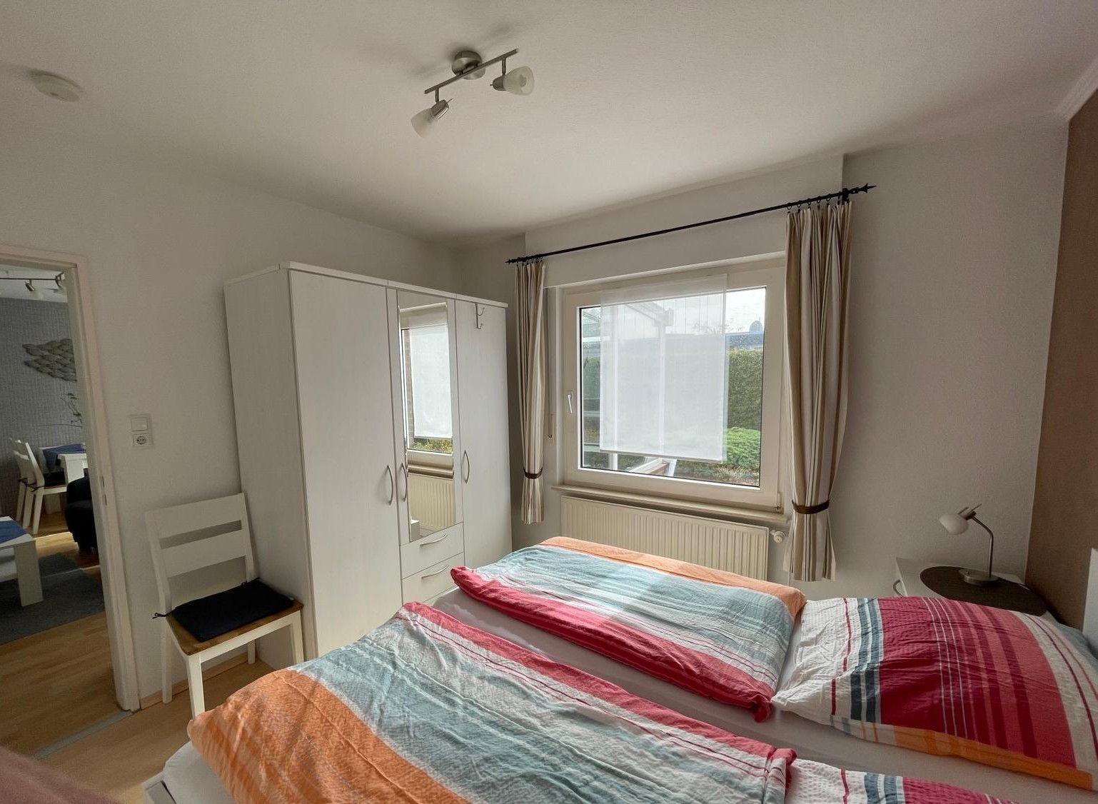 Schlafzimmer mit Doppelbett, Kleiderschrank und Fenster mit Vorhängen.