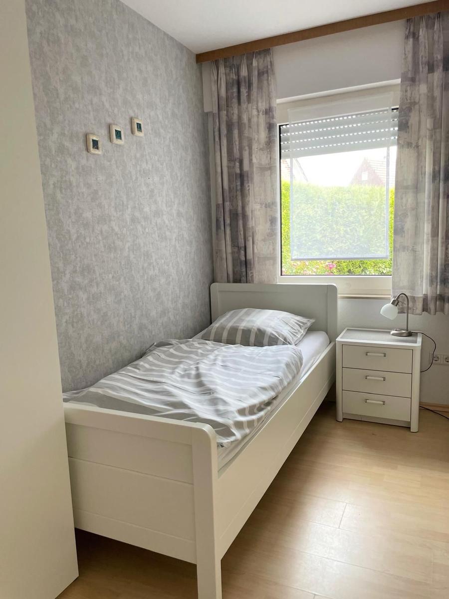 Ein Schlafzimmer mit einem Bett, Nachttisch und Fenster mit Vorhängen.