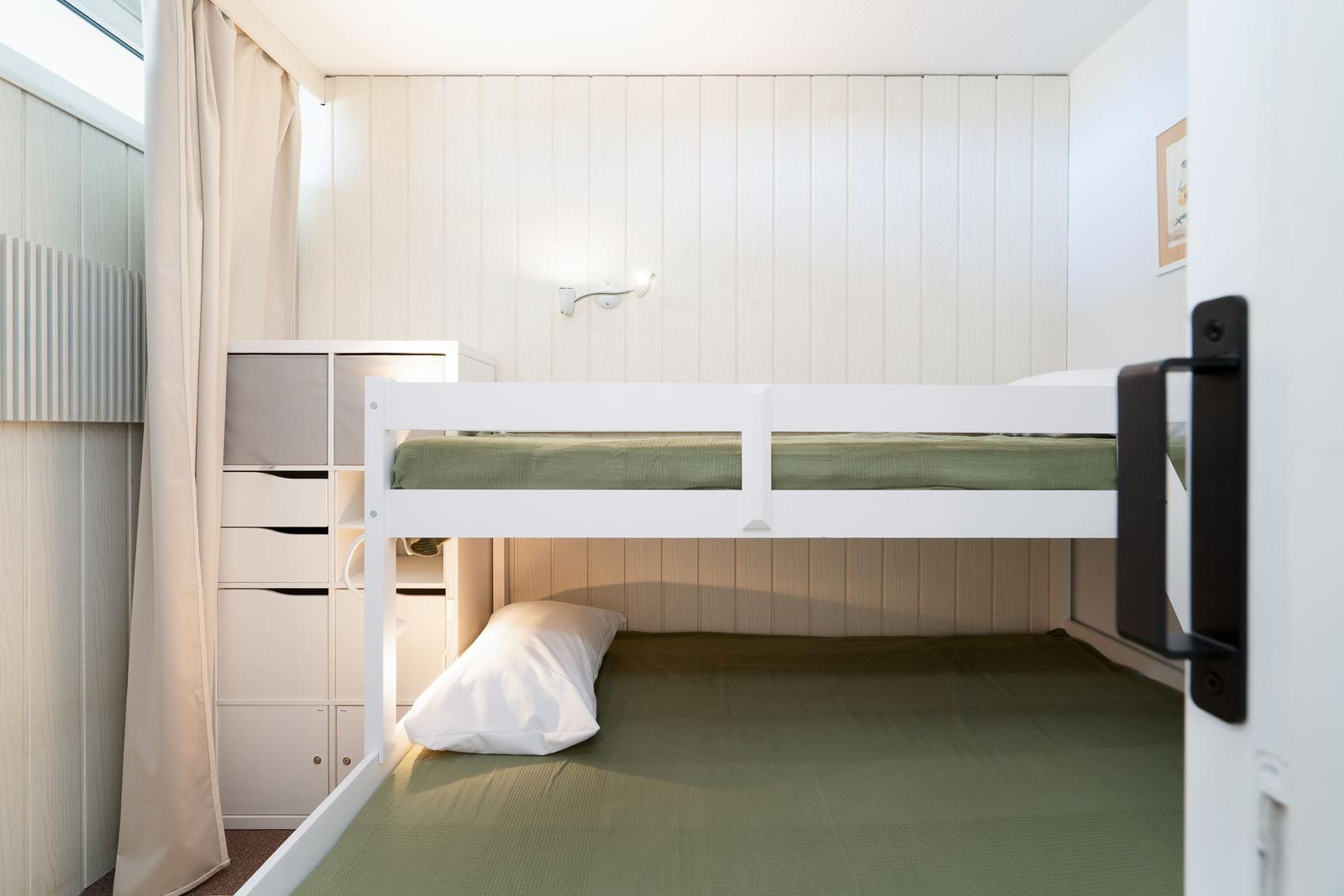 Ein Doppelstockbett mit grüner Bettwäsche und weißer Matratze. An der Wand hängt eine Wandlampe.