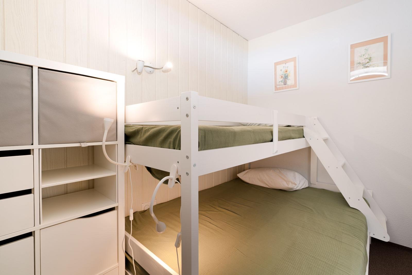 Zimmer mit Doppelstockbett, Schrank und Wandbeleuchtung.