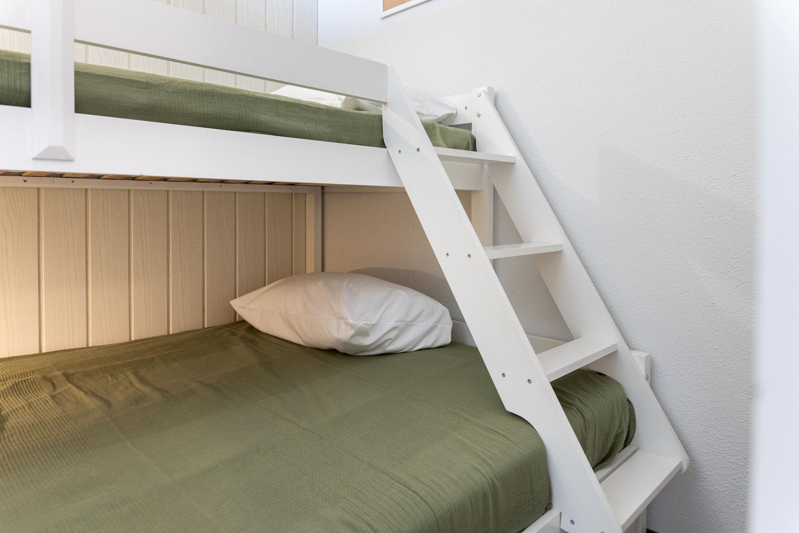Ein weißes Doppelbett mit grüner Bettwäsche und einer Leiter.