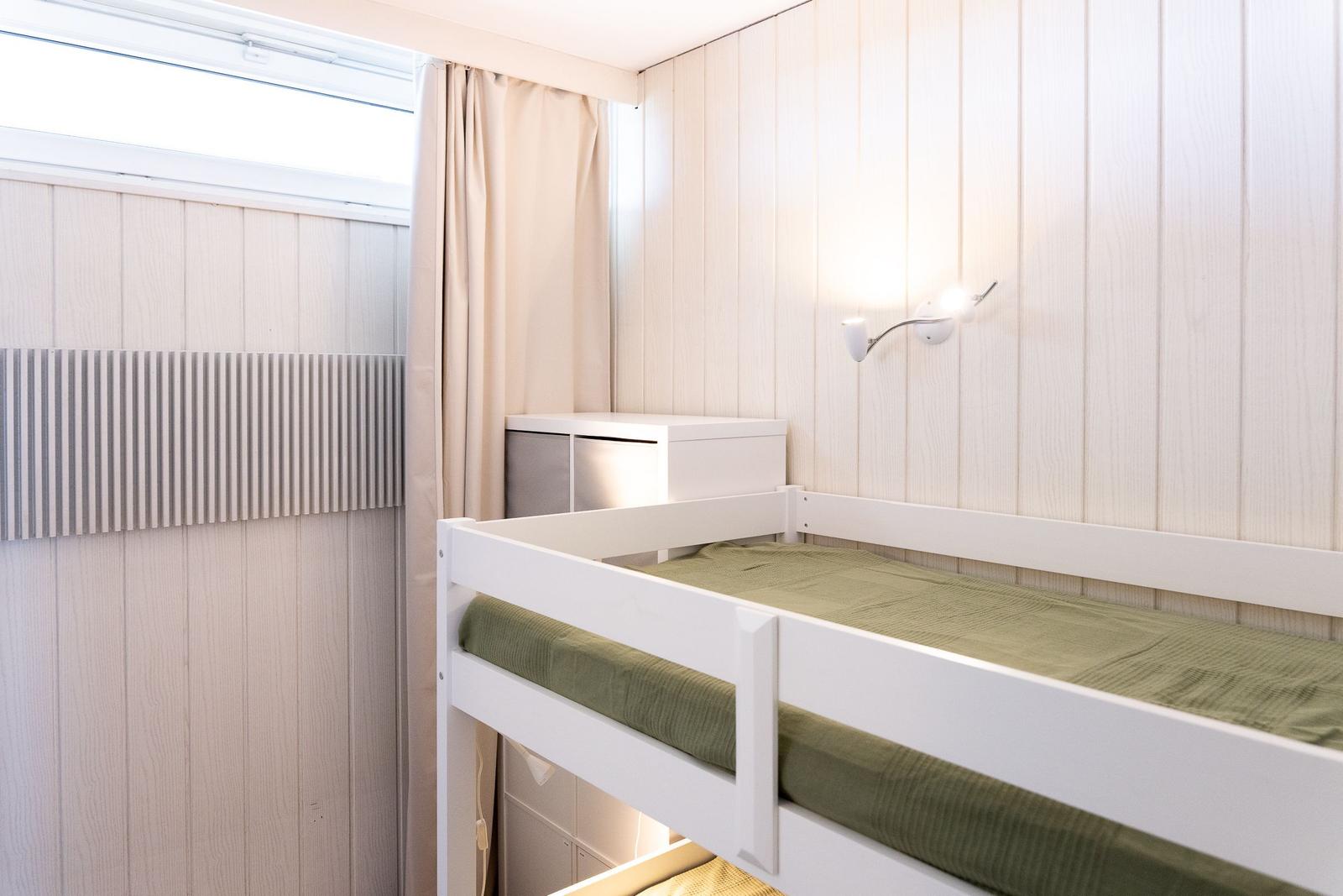 Schlafzimmer mit Doppelstockbett, Wandlampe und Fenster mit Vorhang.