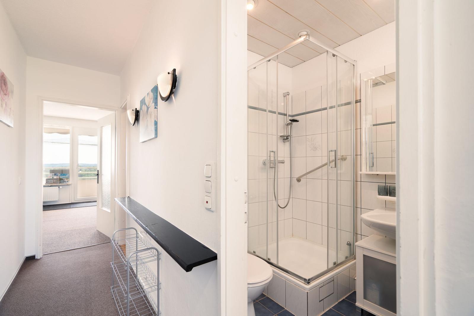 Badezimmer mit Dusche und Waschbecken. Flur mit Schrank und Blick auf Balkon.