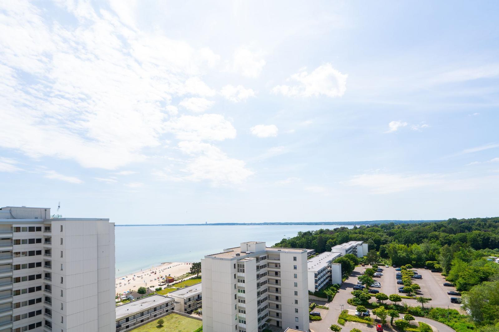 Panoramablick auf Strand, See und Wohnhäuser unter blauem Himmel mit weißen Wolken.