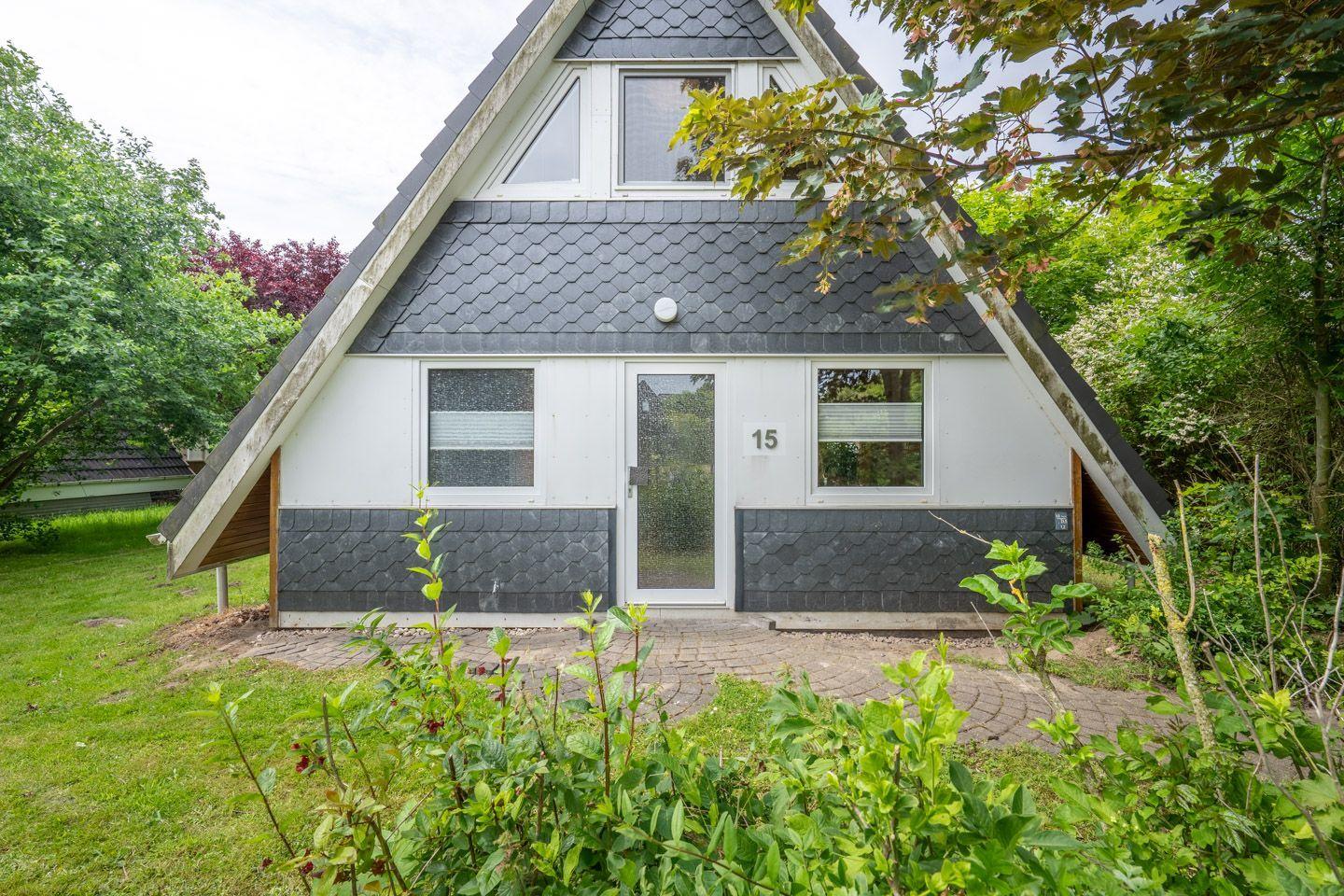 Haus mit schwarzem Dach und weißer Fassade, umgeben von Grünflächen und Bäumen.