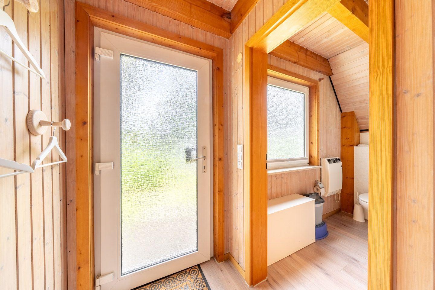 Hölzerner Eingangsbereich mit Glastür und angrenzender Toilettenkabine.