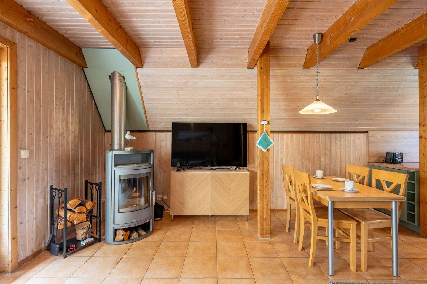Wohn- und Essbereich mit Holzvertäfelung, Kaminofen, TV und Tisch mit Stühlen.