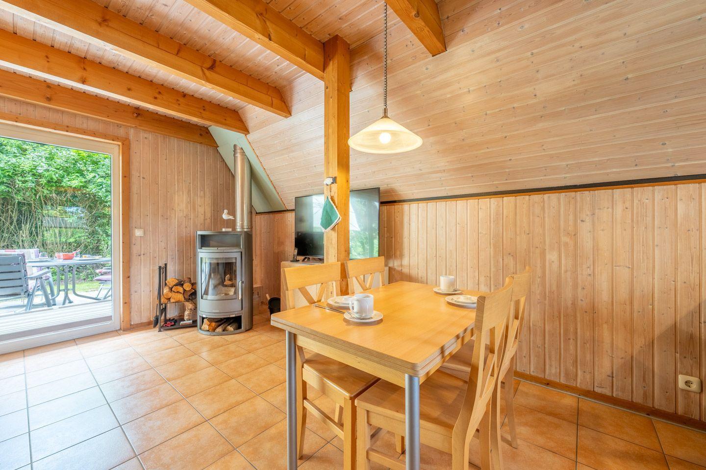 Esszimmer mit Holztisch, Stühlen und Kaminofen. Durchgang zum Garten.