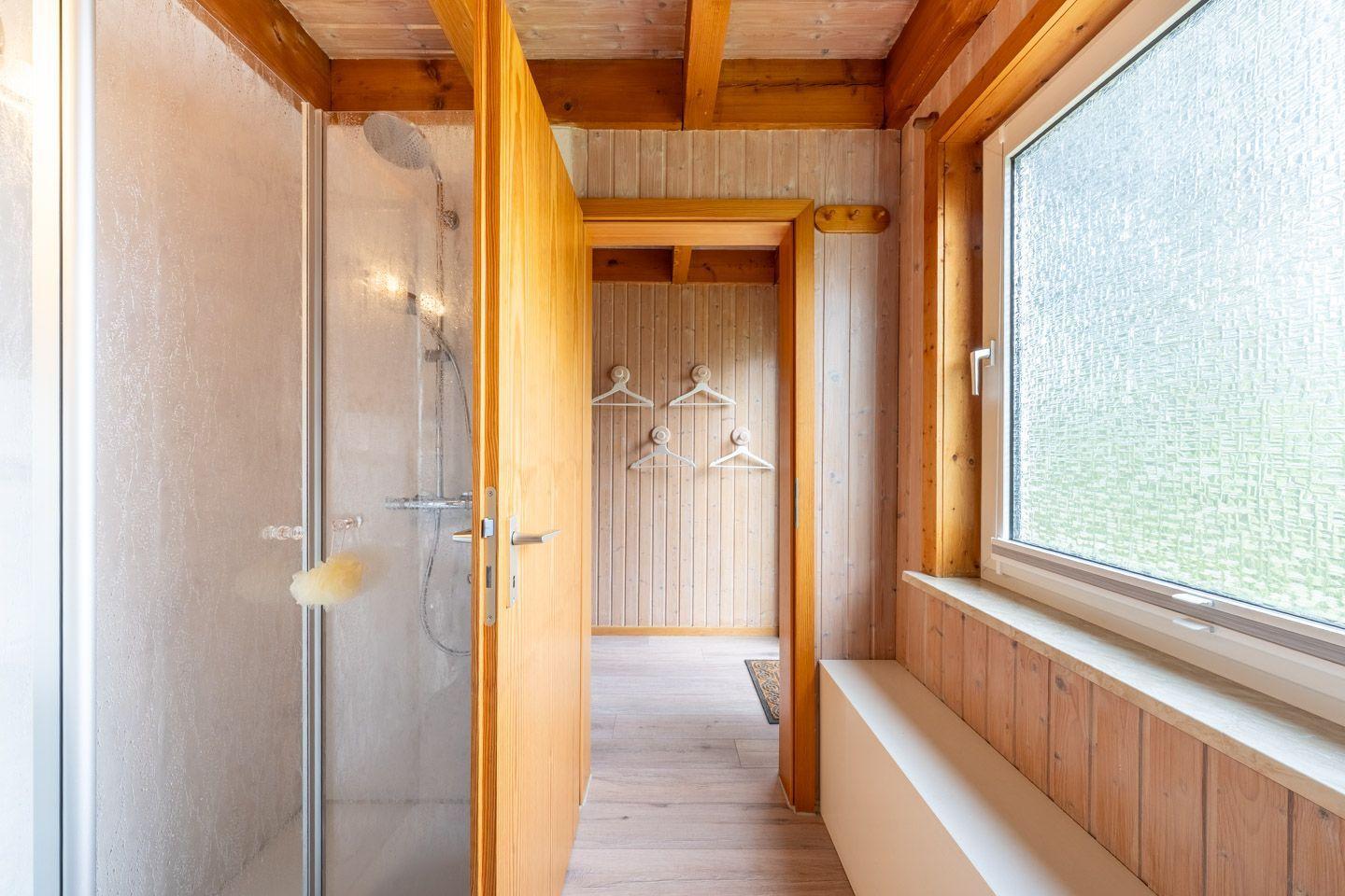Dusche mit Glaswand, Holzverkleidung und Fenster mit Sitzbank.