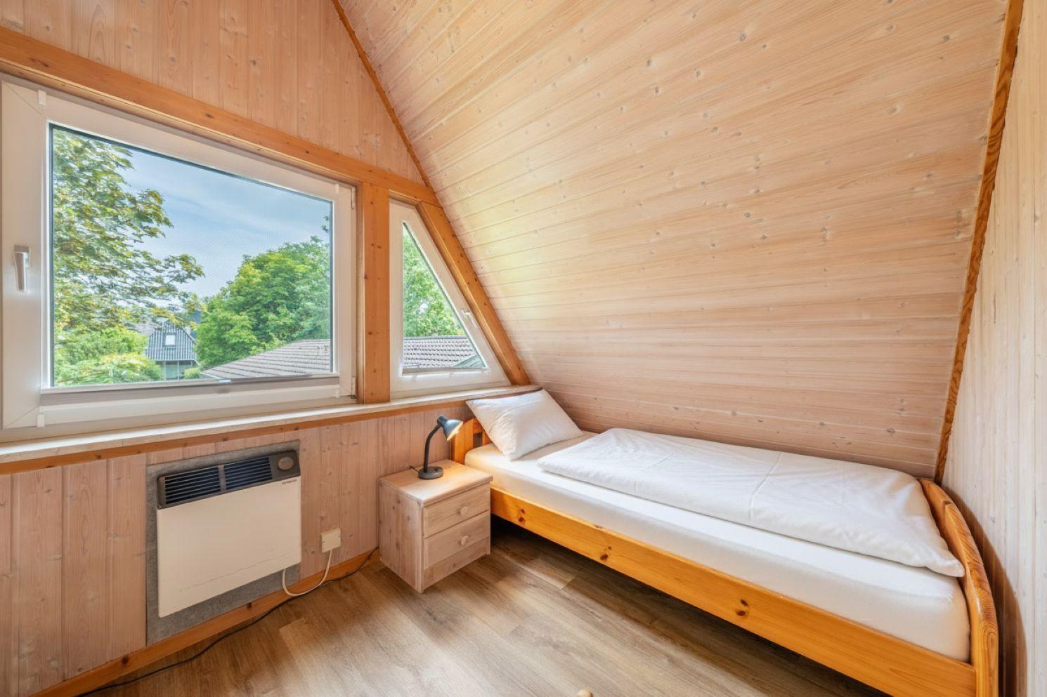 Ein Schlafzimmer mit Holzwand, Doppelbett, Nachttisch und Fenster mit Blick auf Grün.