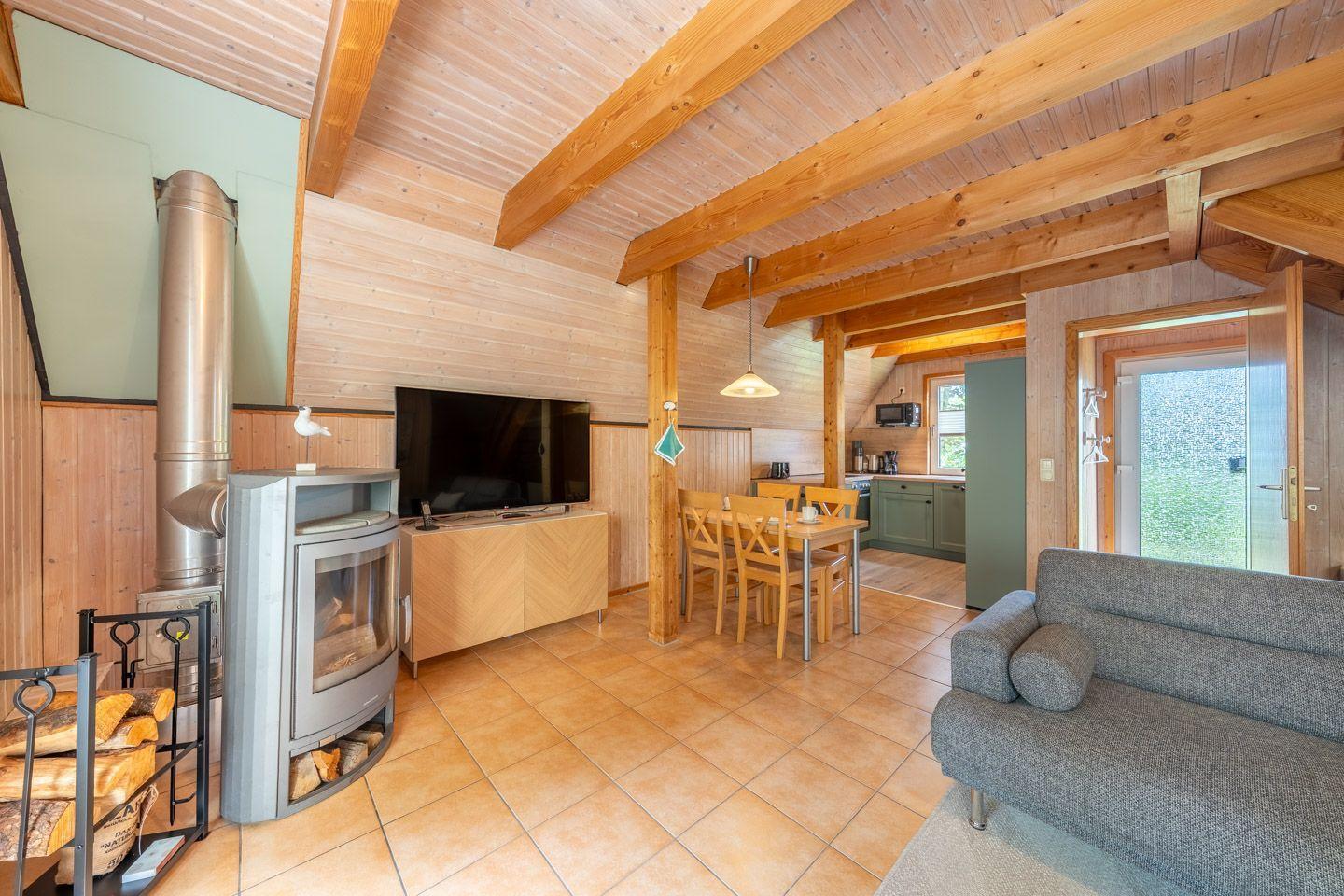 Wohnzimmer mit Kamin, Sofa, Esstisch und Küchenbereich. Holzdecke und -wände.