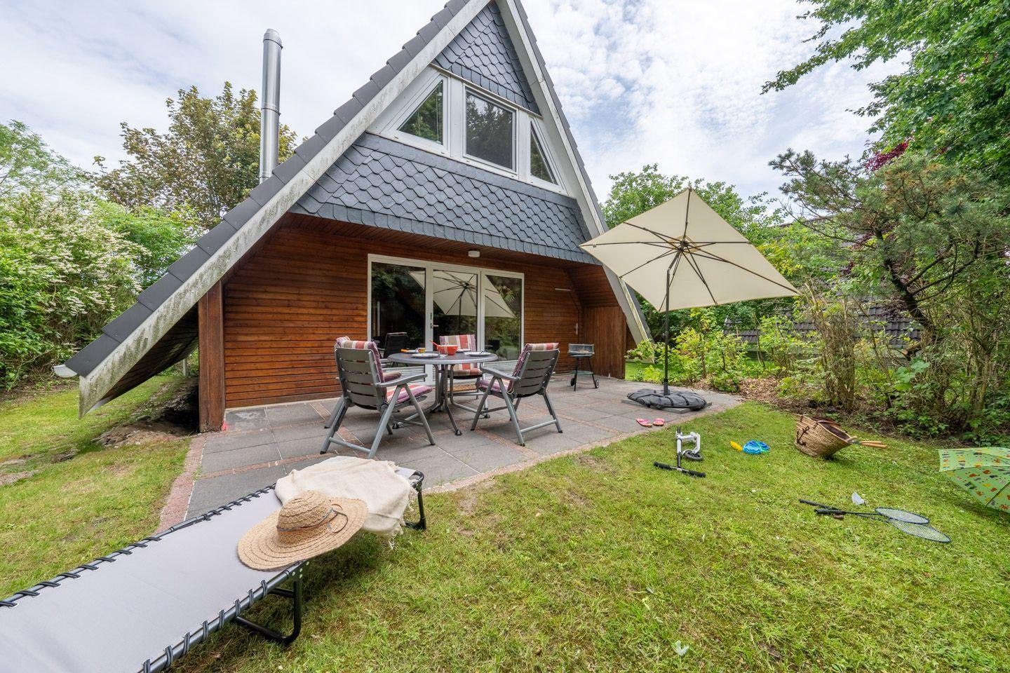 Haus mit Terrasse, Tisch, Stühlen, Sonnenschirm und Liegestuhl im Garten.