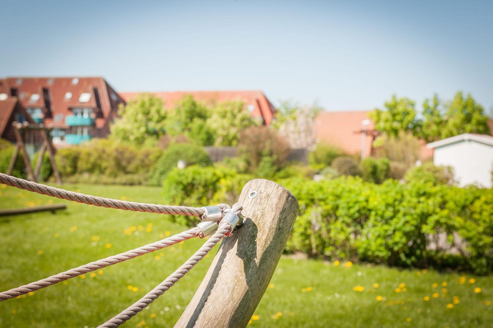 Holzpfosten mit Seil in Garten, Hintergrund mit Häusern und Grün.