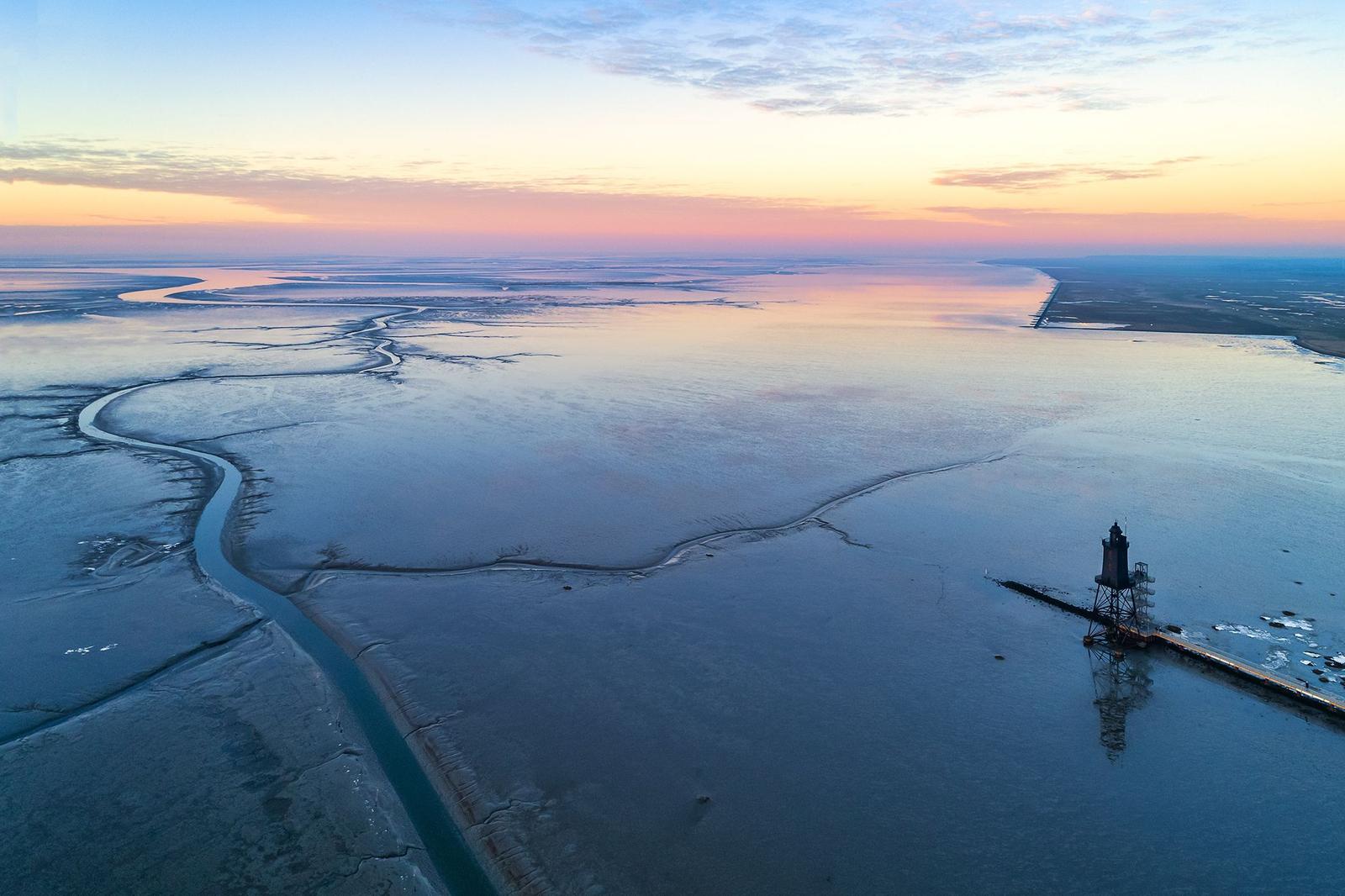 Aerial view of a lighthouse at sunset over a wide estuary with winding waterways.