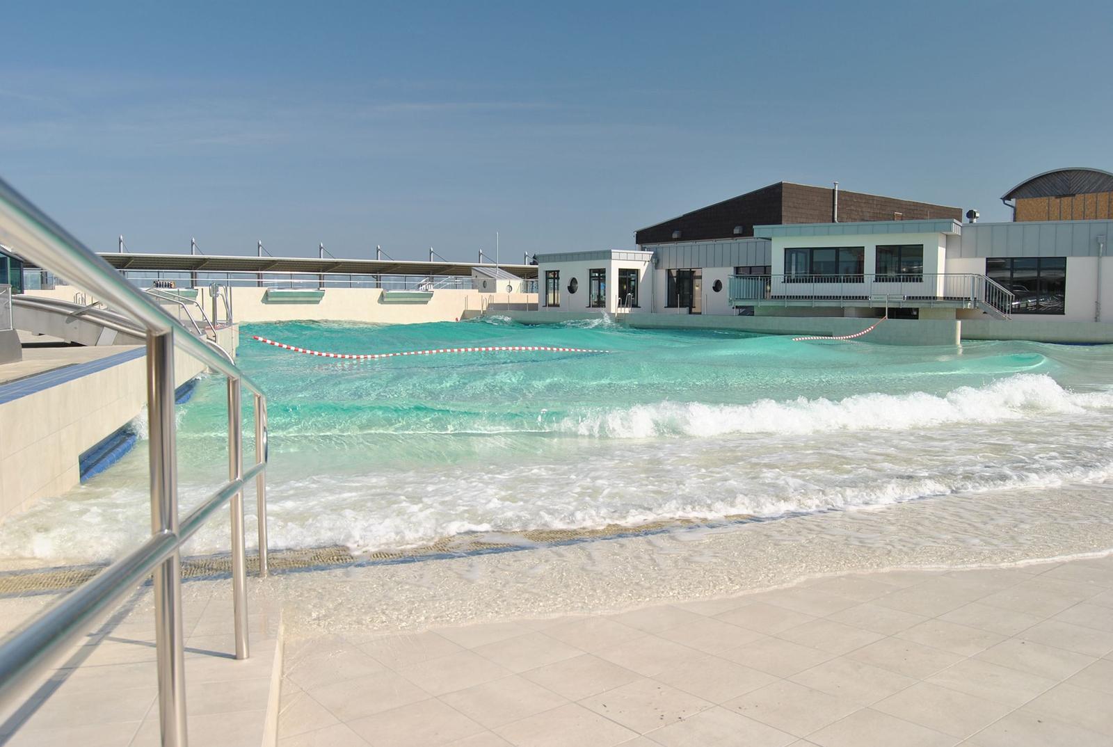 Wellenbad mit moderner Umgebung und Glasfassade. Poolbereich mit Metallgeländer.