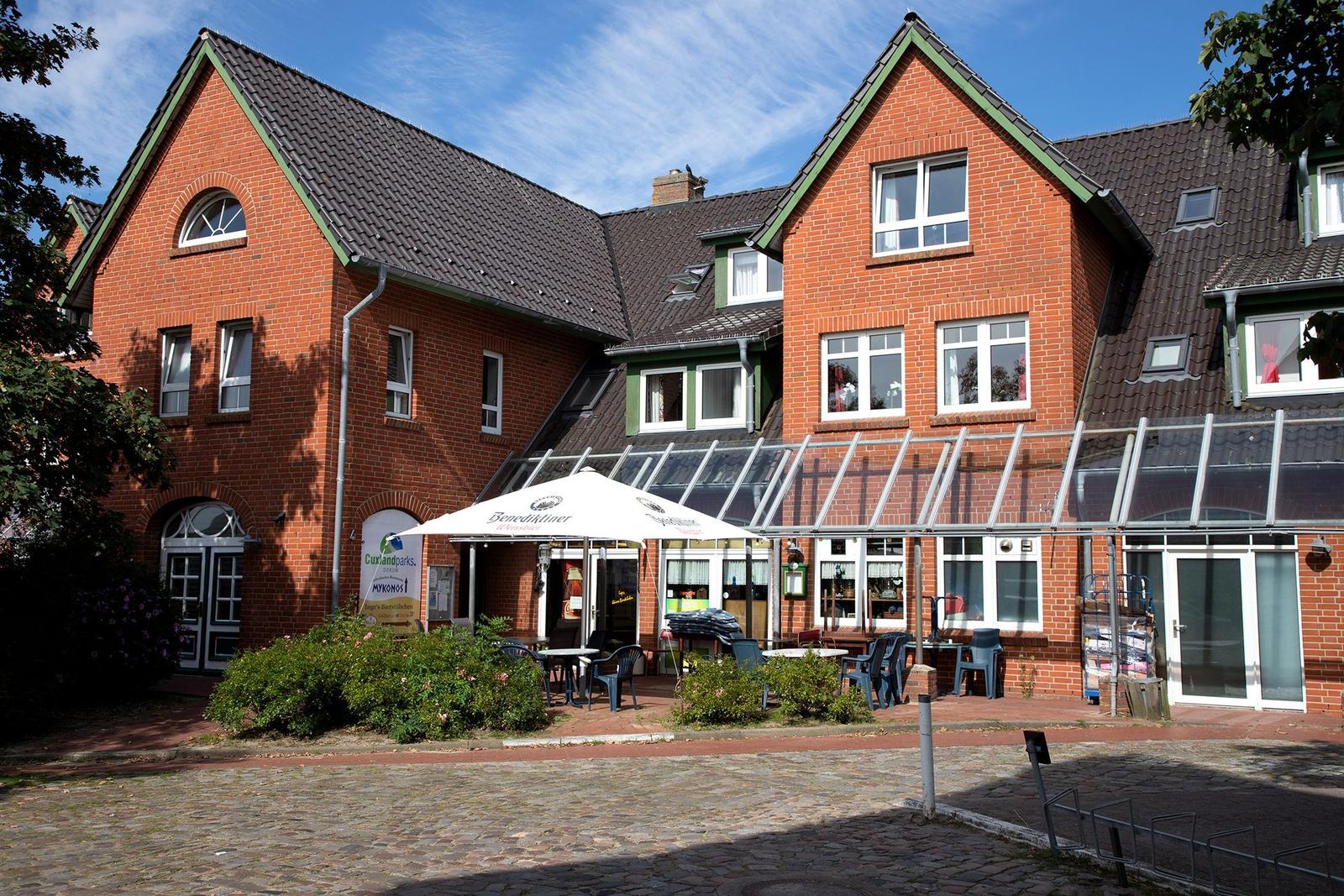 Rotes Backsteinhaus mit Terrasse und Sonnenschirm. Außenbereich mit Tischen und Stühlen.