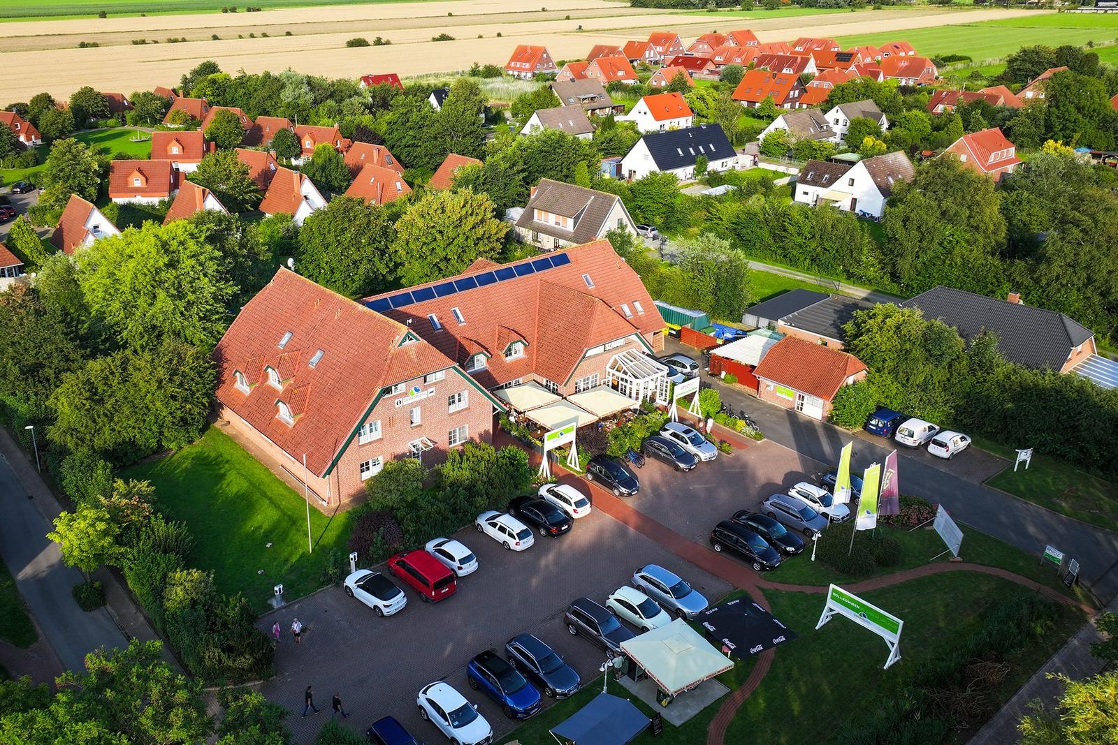 Großes Haus mit rotem Dach, umgeben von Grünflächen und Parkplatz mit Autos.