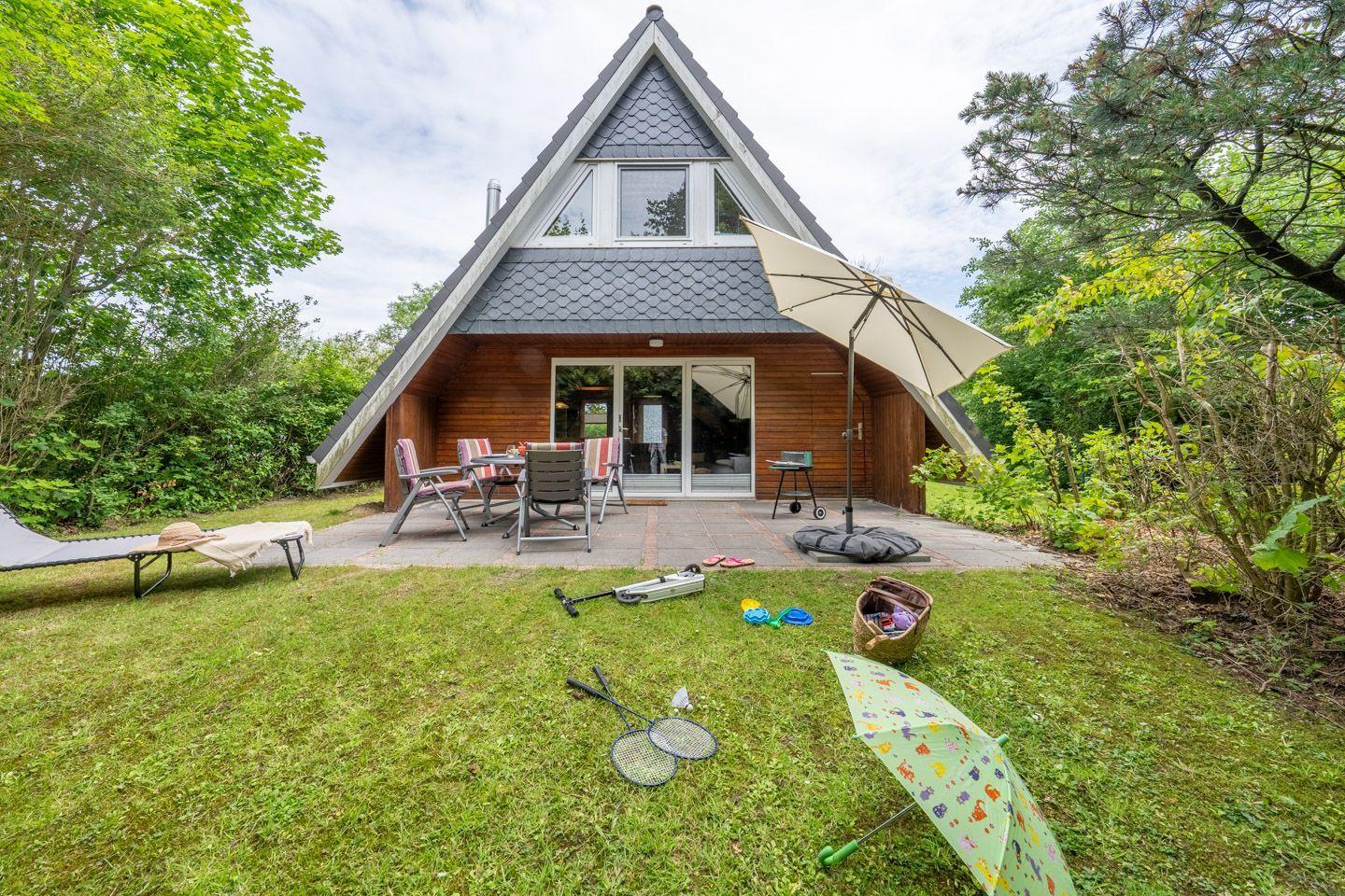 Haus mit Terrasse, Gartenmöbeln und Kinderspielzeug im Gras.