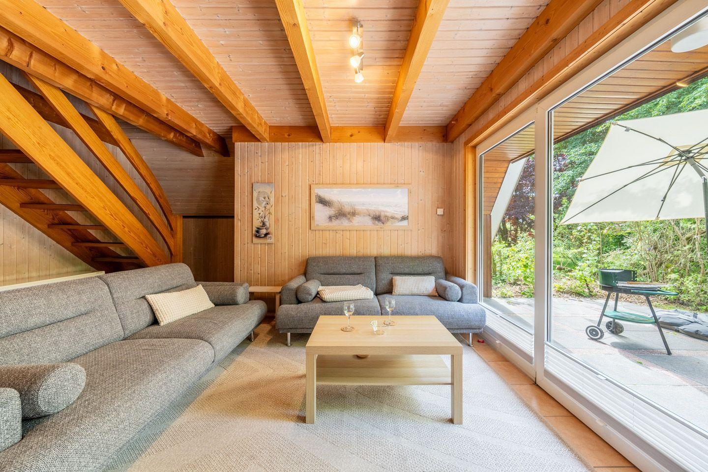 Wohnzimmer mit Holzdecke, Sofa und Blick auf den Garten.