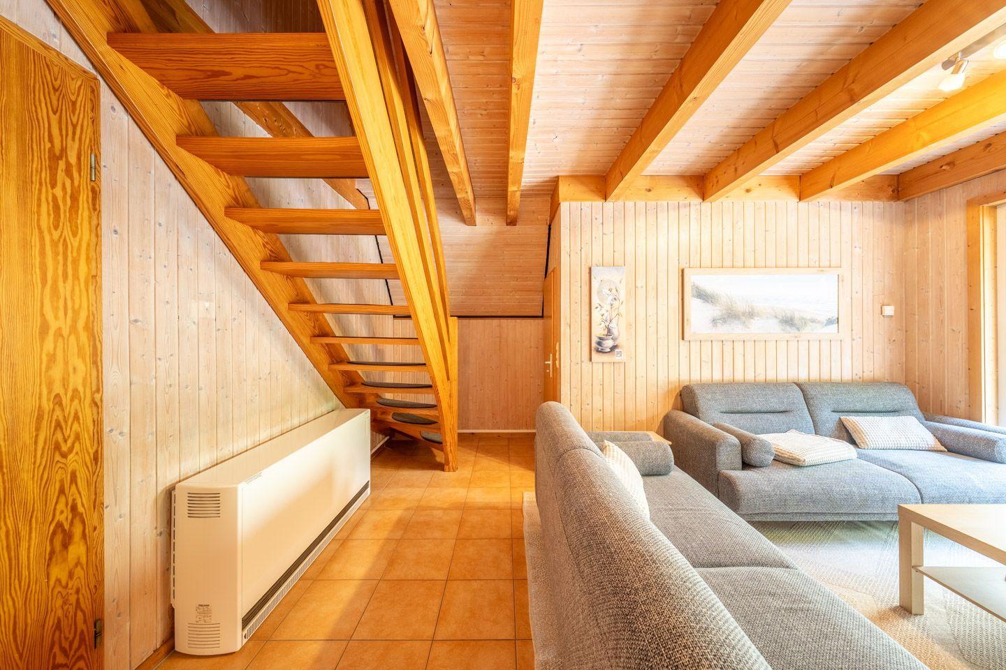 Wohnzimmer mit Holzdecke, Sofa und Treppe zur oberen Etage.
