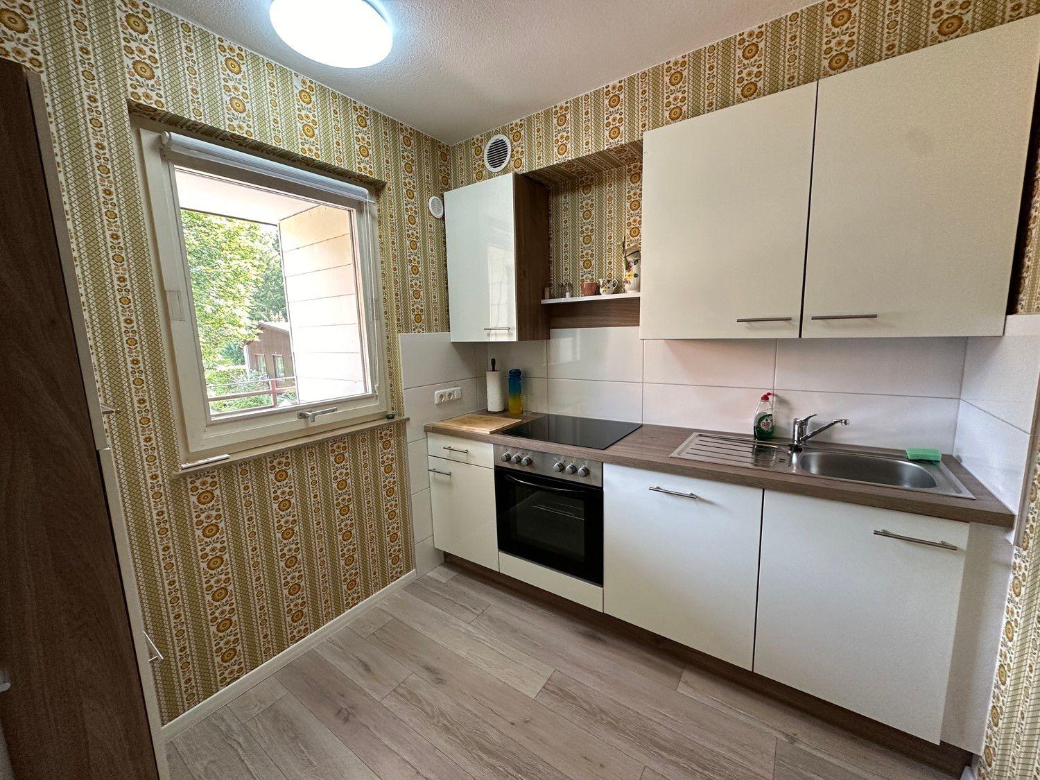 Küche mit weißen Schränken, Holzoberfläche und Fenster mit Blick auf Garten.