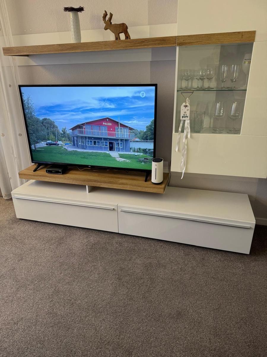 TV auf Holzregal, daneben Glaswand mit Gläsern und Dekoration.