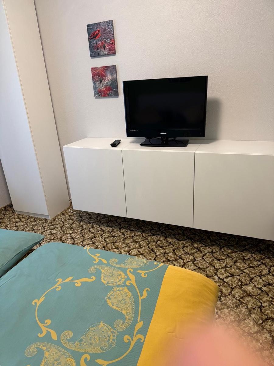 Schlafzimmer mit Bett, Fernseher und Wandbildern.