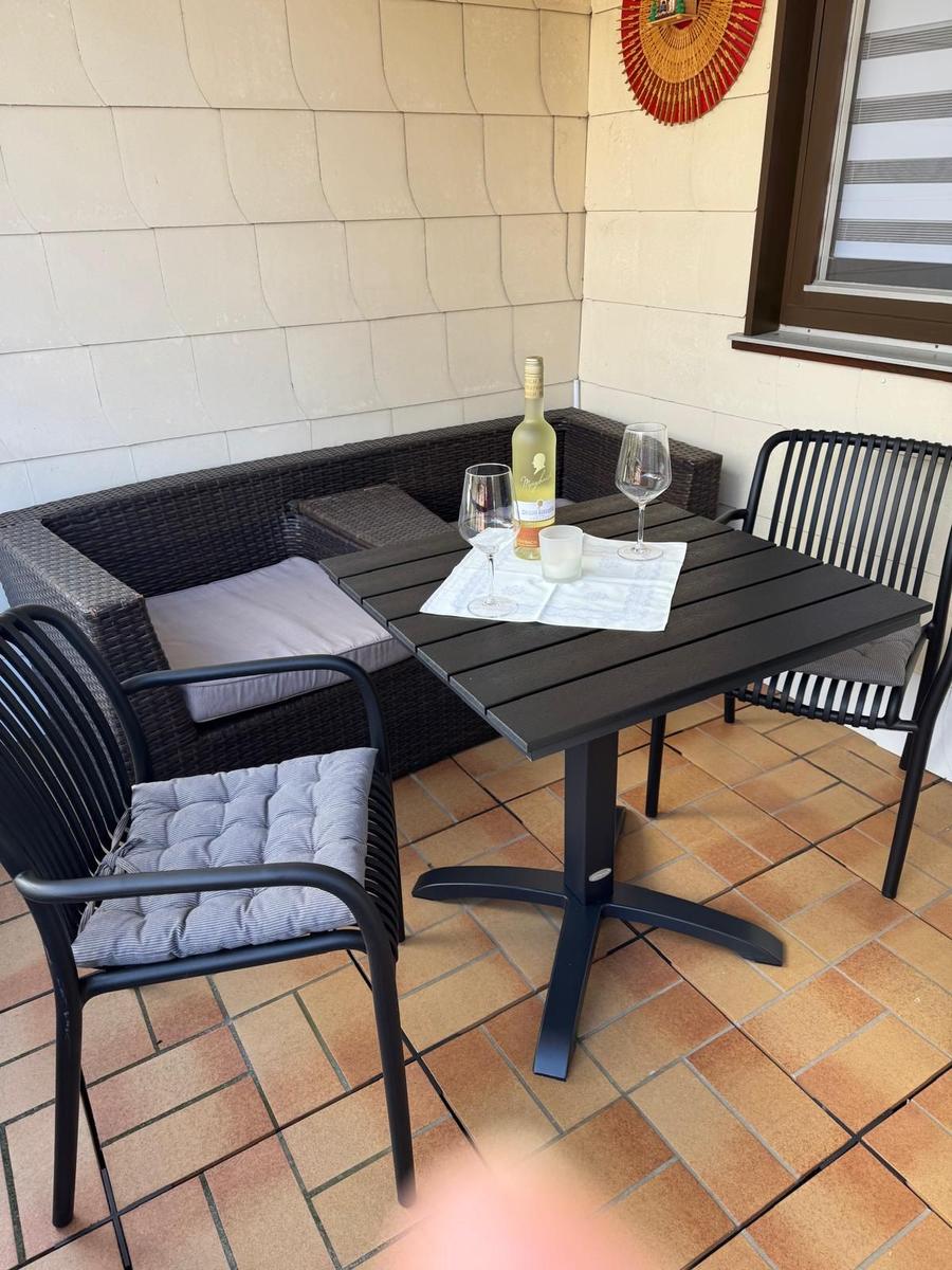 Terrasse mit Tisch, Stühlen und Sitzbank. Auf dem Tisch steht eine Weinflasche und zwei Gläser.